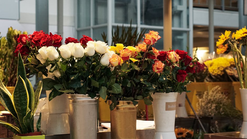 A collection of flower arrangements displayed on a table at a floral shop, featuring a variety of roses in red, white, and orange-pink hues, with some having delicate petals and others with fuller blo